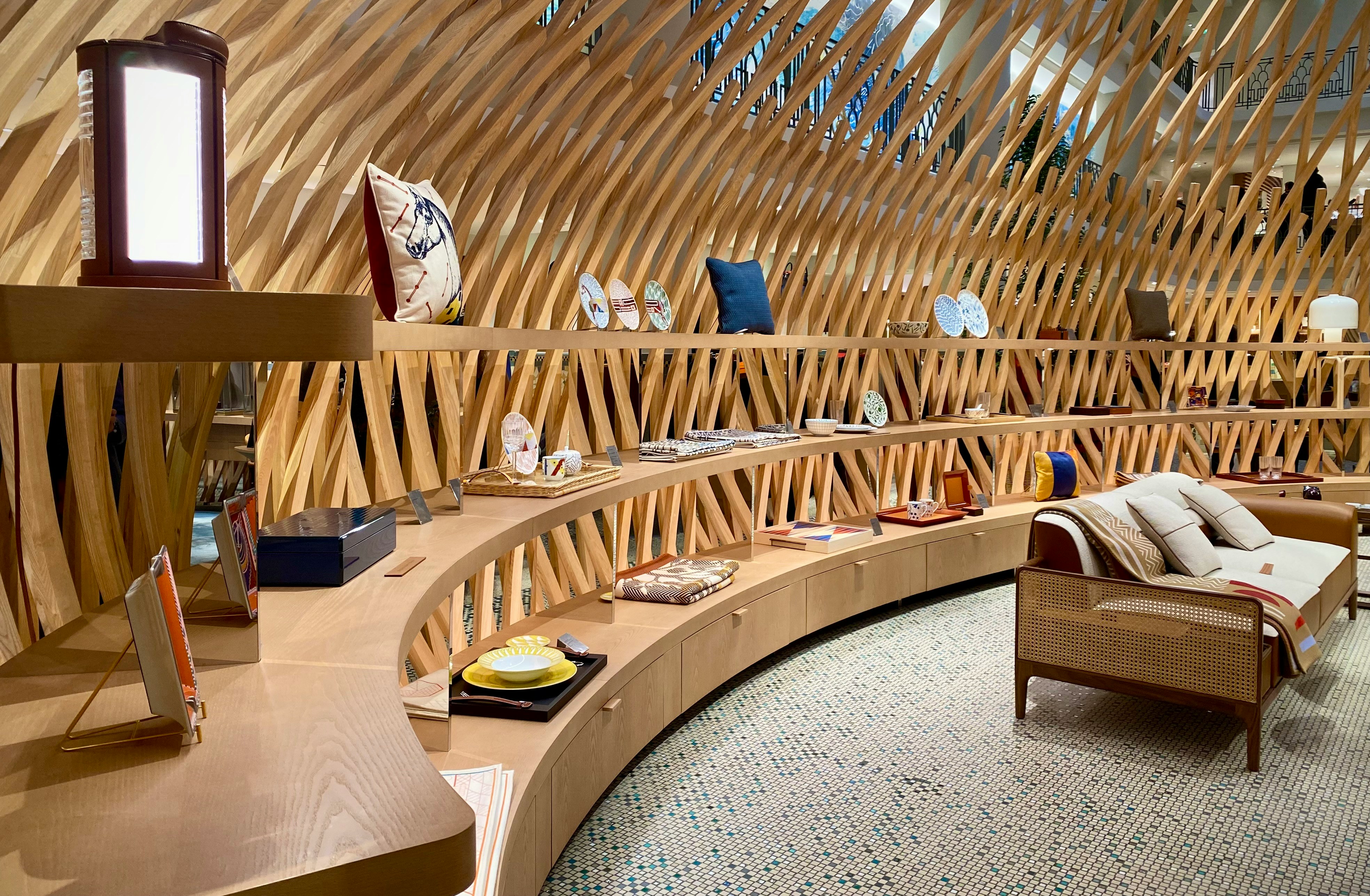 Curved wooden shelves with decorative plates, pillows, and a beige sofa in a modern store interior.